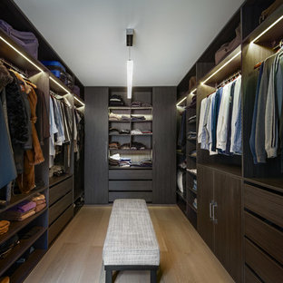 Réalisation d'un grand dressing design neutre avec un placard sans porte, des portes de placard en bois sombre, un sol en bois clair et un sol beige.