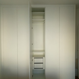 Imagen de armario unisex, moderno, de tamaño medio, con puertas de armario blancas, suelo de madera en tonos medios y suelo marrón