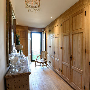 Cette image montre un dressing traditionnel pour une femme avec un placard avec porte à panneau surélevé, des portes de placard en bois brun, un sol en bois clair et un sol beige.