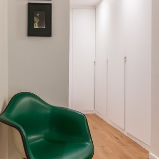 Cette image montre un dressing design neutre avec un placard à porte plane, des portes de placard blanches, un sol en bois brun et un sol marron.