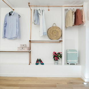 Réalisation d'un grand dressing nordique pour une femme avec un sol en bois clair, un placard sans porte et un sol beige.