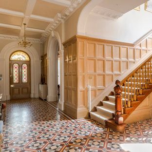 Idées déco pour un hall d'entrée classique avec un mur beige, une porte simple, une porte en bois brun, un sol multicolore, un plafond à caissons et du lambris.