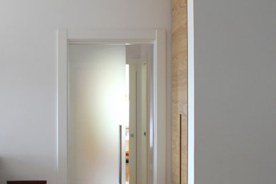 Photo of a large contemporary hallway with white walls, light hardwood flooring, a single front door and a white front door.