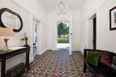他の地域にあるお手頃価格の広いヴィクトリアン調のおしゃれな玄関ロビー (白い壁、磁器タイルの床、白いドア、マルチカラーの床) の写真