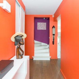 Aménagement d'un grand hall d'entrée contemporain avec un mur orange et un sol en bois foncé.