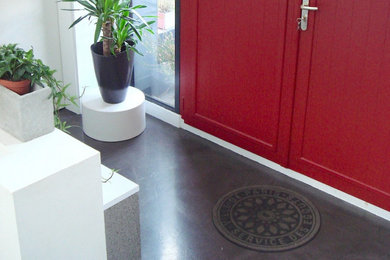Aménagement d'un hall d'entrée contemporain avec un mur blanc, sol en béton ciré, une porte simple, une porte rouge et un sol gris.