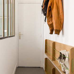 Réalisation d'une petit entrée design avec un couloir, un mur blanc, béton au sol, une porte simple, une porte blanche et un sol gris.