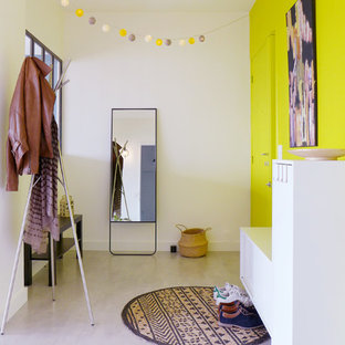 Idées déco pour un grand hall d'entrée contemporain avec un mur jaune, béton au sol, une porte simple, une porte jaune et un sol gris.