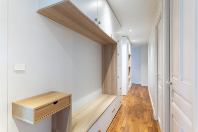 Cette image montre une entrée craftsman de taille moyenne avec un couloir, un mur blanc, parquet clair, une porte blanche et un sol marron.