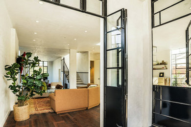 Großer Eingang mit weißer Wandfarbe, dunklem Holzboden und Haustür aus Glas in Los Angeles