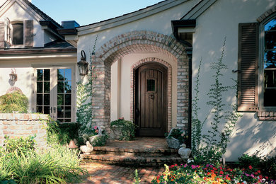 Пример оригинального дизайна: маленькая входная дверь в средиземноморском стиле с бежевыми стенами, одностворчатой входной дверью и входной дверью из темного дерева для на участке и в саду