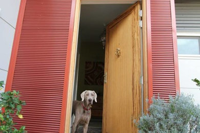 Imagen de puerta principal actual con paredes rojas, suelo de cemento, puerta pivotante y puerta de madera clara