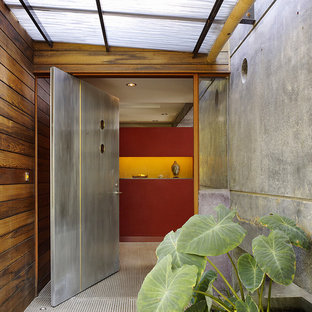 Immagine di una grande porta d'ingresso contemporanea con pareti rosse, pavimento in cemento, una porta a pivot e una porta in metallo