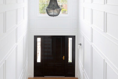 Modelo de puerta principal tradicional grande con paredes blancas, suelo de madera clara, puerta simple, puerta negra y boiserie