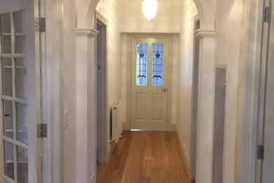 Modelo de entrada tradicional con suelo de madera en tonos medios y puerta blanca