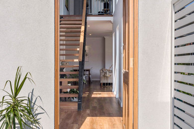 На фото: маленькая входная дверь в современном стиле с белыми стенами, полом из ламината, одностворчатой входной дверью, входной дверью из светлого дерева и коричневым полом для на участке и в саду