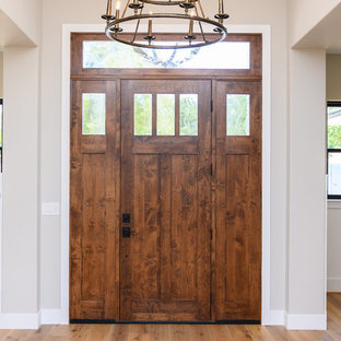 Cette image montre une petit porte d'entrée rustique avec un mur beige, une porte simple, une porte en bois foncé, un sol en bois clair et un sol beige.