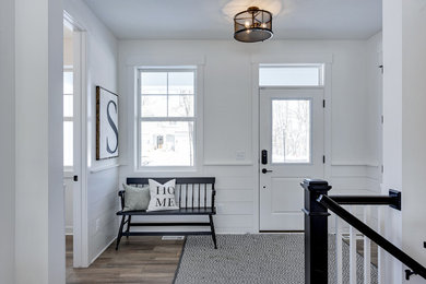 This is an example of a medium sized farmhouse foyer in Minneapolis with white walls, laminate floors, a single front door, a white front door, brown floors and feature lighting.