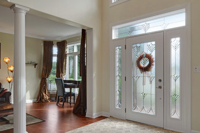 Idee per un grande ingresso classico con pavimento in legno massello medio, una porta singola, una porta bianca, pareti beige e pavimento marrone