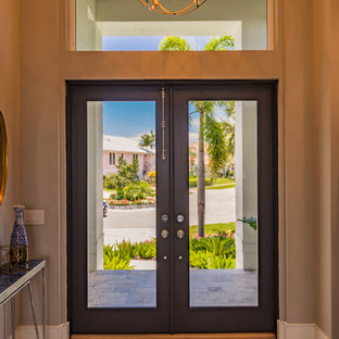 Exemple d'un hall d'entrée chic de taille moyenne avec un mur beige, un sol en bois clair, une porte double, une porte en verre et un sol marron.