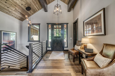 Example of a mountain style medium tone wood floor, brown floor and exposed beam single front door design in Boise with gray walls and a dark wood front door