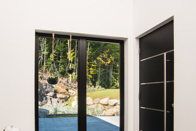 Cette image montre une porte d'entrée design de taille moyenne avec un mur blanc, un sol en carrelage de porcelaine, une porte simple, une porte noire et un sol marron.