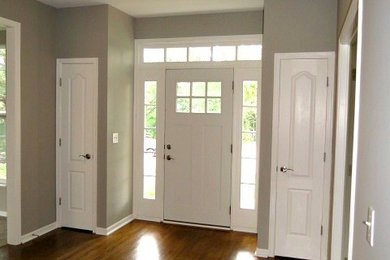 Modelo de entrada clásica con paredes grises, suelo de madera oscura, puerta simple y puerta blanca