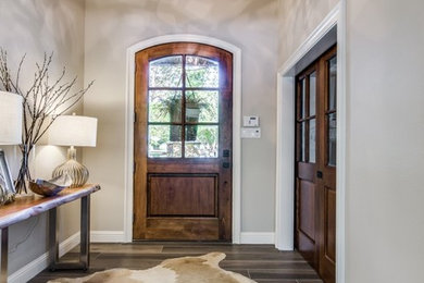 ダラスにある中くらいなトランジショナルスタイルのおしゃれな玄関ドア (グレーの壁、木目調のドア、茶色い床、磁器タイルの床) の写真