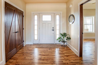 Example of a large farmhouse light wood floor and brown floor entryway design in Denver with beige walls and a white front door