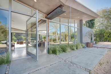 This is an example of an expansive retro front door in Los Angeles with concrete flooring, a pivot front door, a glass front door and grey floors.