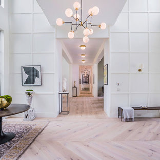 Réalisation d'un très grand hall d'entrée design avec un mur blanc, un sol en bois clair, une porte métallisée et une porte double.