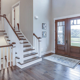 Aménagement d'un très grand hall d'entrée campagne avec un mur gris, un sol en bois brun, une porte double et une porte en bois brun.