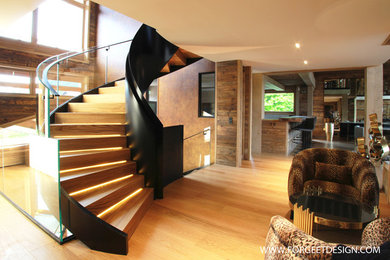 Exemple d'un grand escalier courbe tendance avec des marches en bois, des contremarches en bois et un garde-corps en verre.