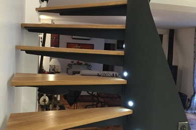 Ejemplo de escalera curva contemporánea de tamaño medio con escalones de madera y barandilla de metal