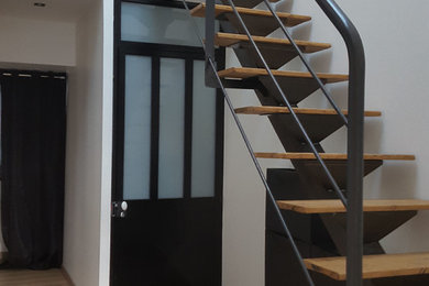 На фото: угловая металлическая лестница среднего размера в стиле лофт с деревянными ступенями и металлическими перилами с
