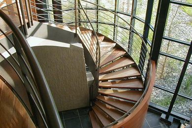 Cette image montre un escalier sans contremarche courbe design de taille moyenne avec des marches en bois et un garde-corps en métal.