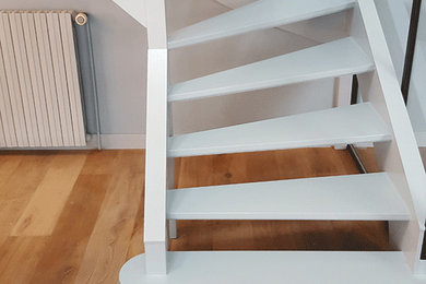 Cette image montre un escalier sans contremarche avec des marches en bois peint et un garde-corps en verre.
