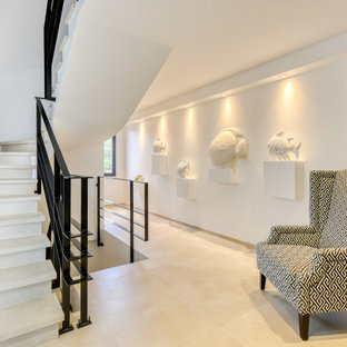 Idee per una grande scala a "U" minimal con pedata in pietra calcarea, alzata in cemento e parapetto in metallo