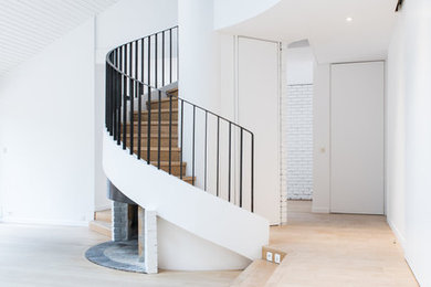 Idée de décoration pour un grand escalier courbe design avec des marches en bois, des contremarches en bois et un garde-corps en métal.