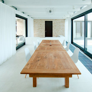 Foto di una grande sala da pranzo aperta verso il soggiorno minimal con pareti bianche, pavimento in gres porcellanato, camino classico e cornice del camino piastrellata