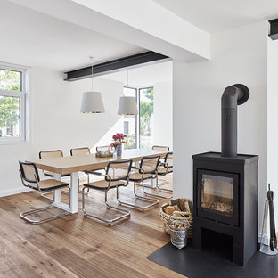 Immagine di una sala da pranzo aperta verso il soggiorno nordica di medie dimensioni con pareti bianche, parquet chiaro e stufa a legna