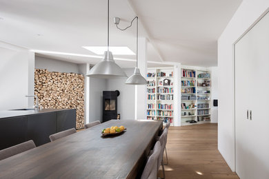 Offenes, Mittelgroßes Modernes Esszimmer mit weißer Wandfarbe, braunem Holzboden, Kaminofen, Kaminumrandung aus Metall und braunem Boden in Berlin