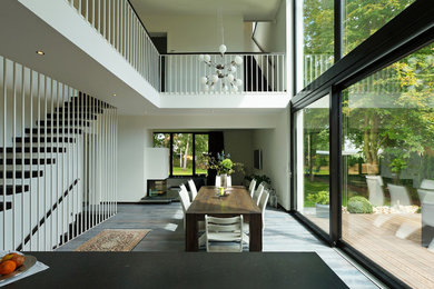 Exemple d'une grande salle à manger ouverte sur le salon tendance avec un mur blanc, une cheminée double-face, un manteau de cheminée en plâtre et parquet clair.