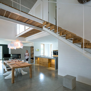 Esempio di una grande sala da pranzo aperta verso la cucina contemporanea con pareti bianche, pavimento in cemento, camino bifacciale, cornice del camino in cemento e pavimento grigio