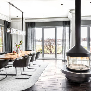 Mittelgroßes Klassisches Esszimmer mit grauer Wandfarbe, Keramikboden, Kaminofen, Kaminumrandung aus Metall und braunem Boden in Berlin