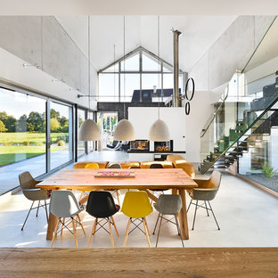 Modelo de comedor actual, extra grande, abierto, con paredes grises, suelo de cemento, chimenea de esquina, marco de chimenea de yeso y suelo gris