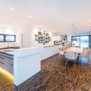 Foto di una grande sala da pranzo aperta verso la cucina contemporanea con pareti bianche, pavimento in bambù, camino bifacciale, cornice del camino in intonaco e pavimento marrone