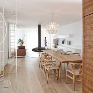 Cette image montre une très grand salle à manger ouverte sur le salon design avec un sol en bois clair, un manteau de cheminée en métal et un mur blanc.