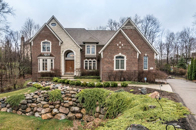 Large and beige traditional two floor brick detached house in Detroit with a shingle roof.