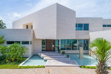 Large modern beige two-story stone flat roof idea in Miami with a mixed material roof